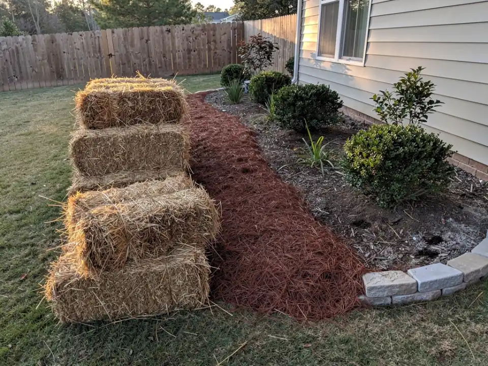 Bales of long-leaf pine straw beside a planting bed that is half covered.