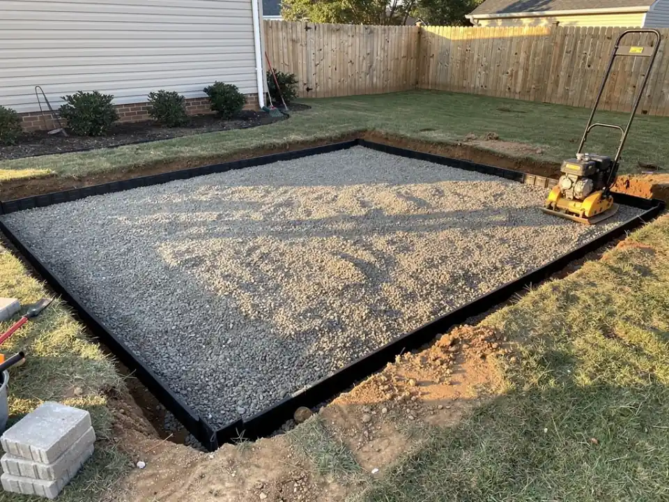 Compacted crushed gravel base with an edge restraint and a plate compactor at one corner.