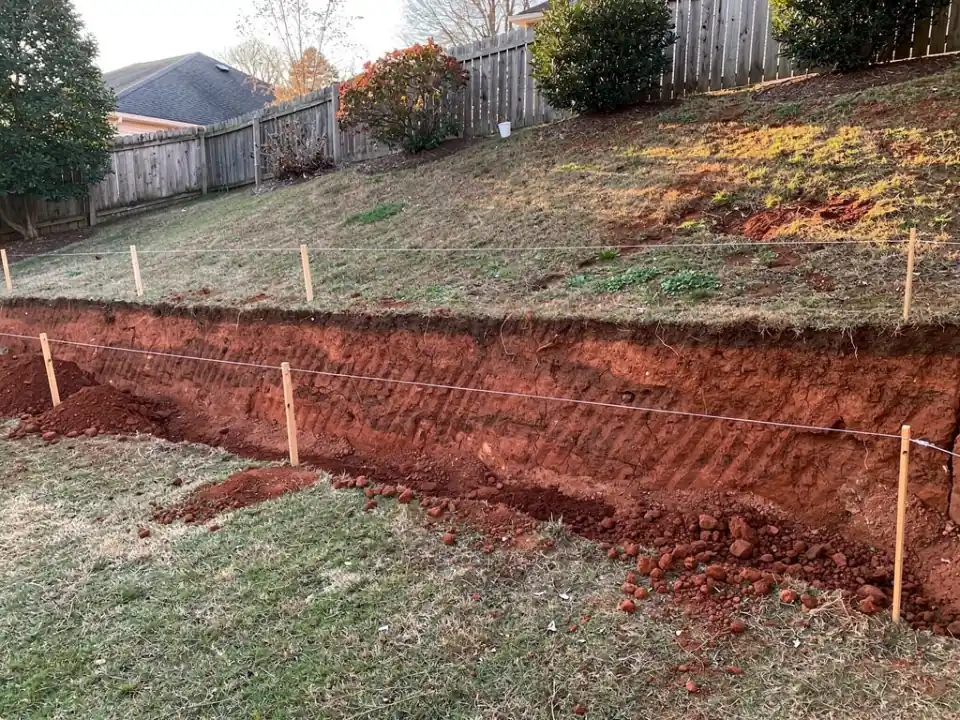 Level footing trench cut at the base of a red clay slope, with string lines above it.