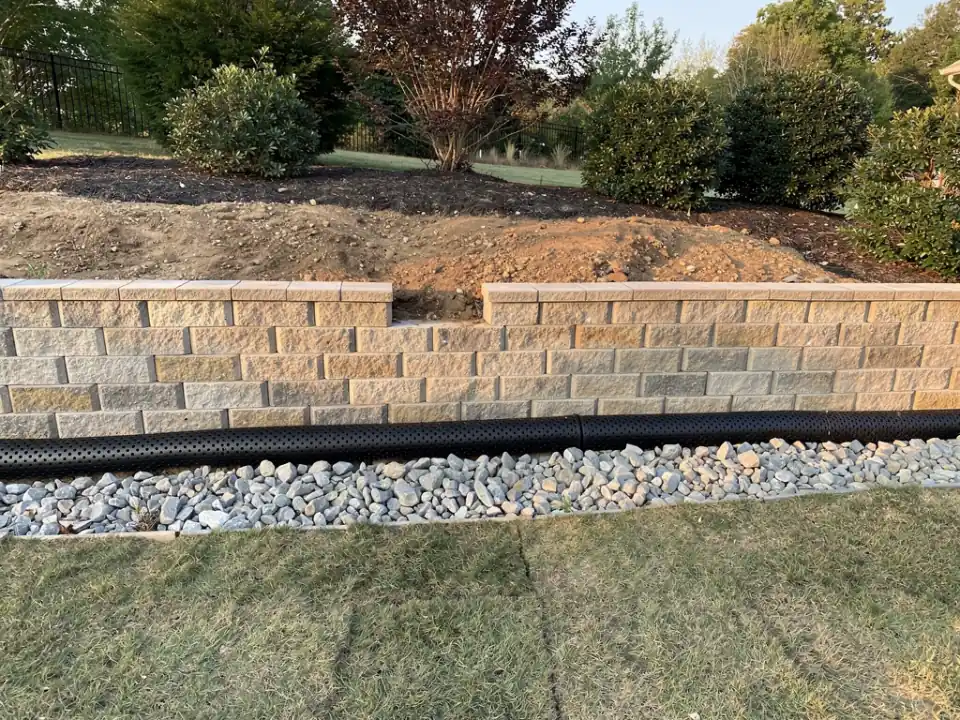 Half-built block wall with perforated drain pipe and washed drainage stone packed behind it.