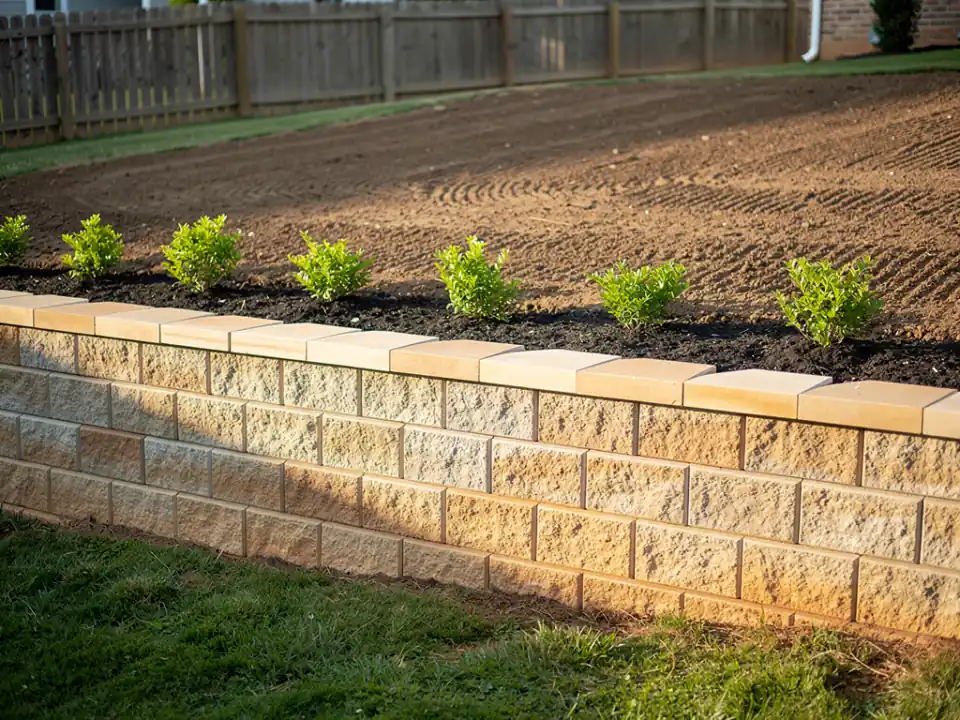 Finished retaining wall with capstones, graded soil and new shrubs planted above.