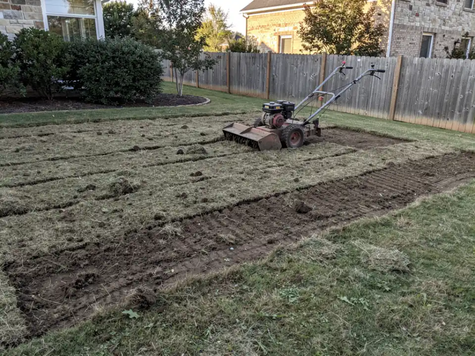 An old patchy lawn stripped and rolled up in strips, with a sod cutter parked at the edge.