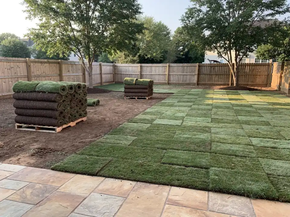 Pallets of sod beside a yard half covered in tight, staggered rows of new turf.